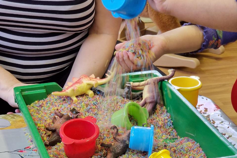 Child playing with coloured rice and toys in box