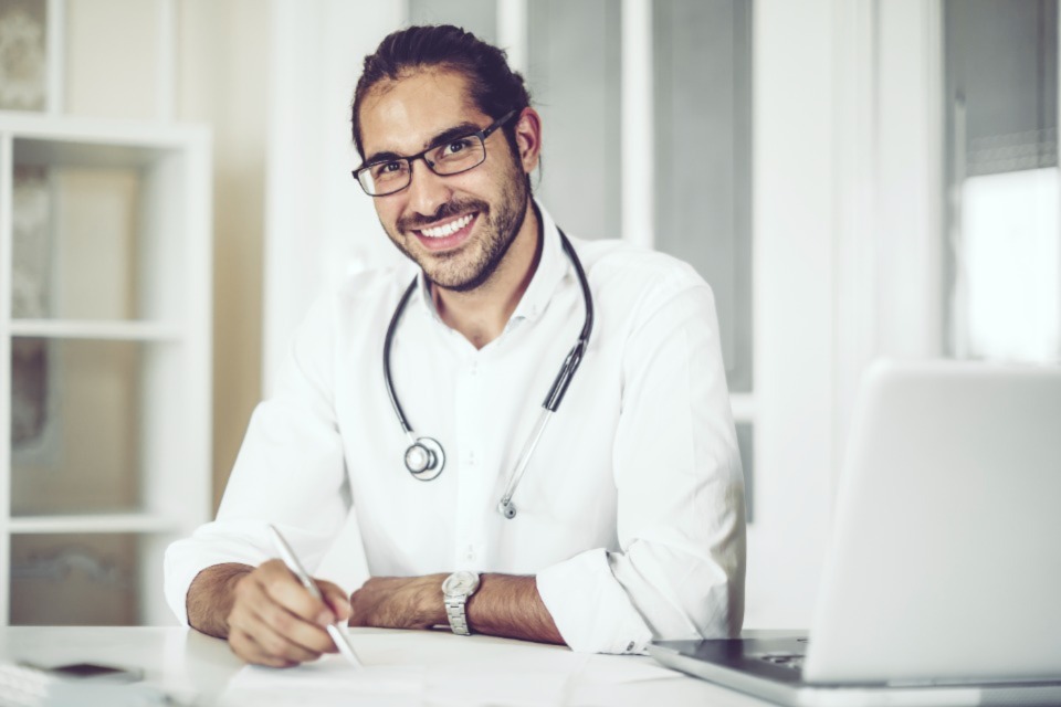 Male medical professional sitting at desk with pen and paper smiling