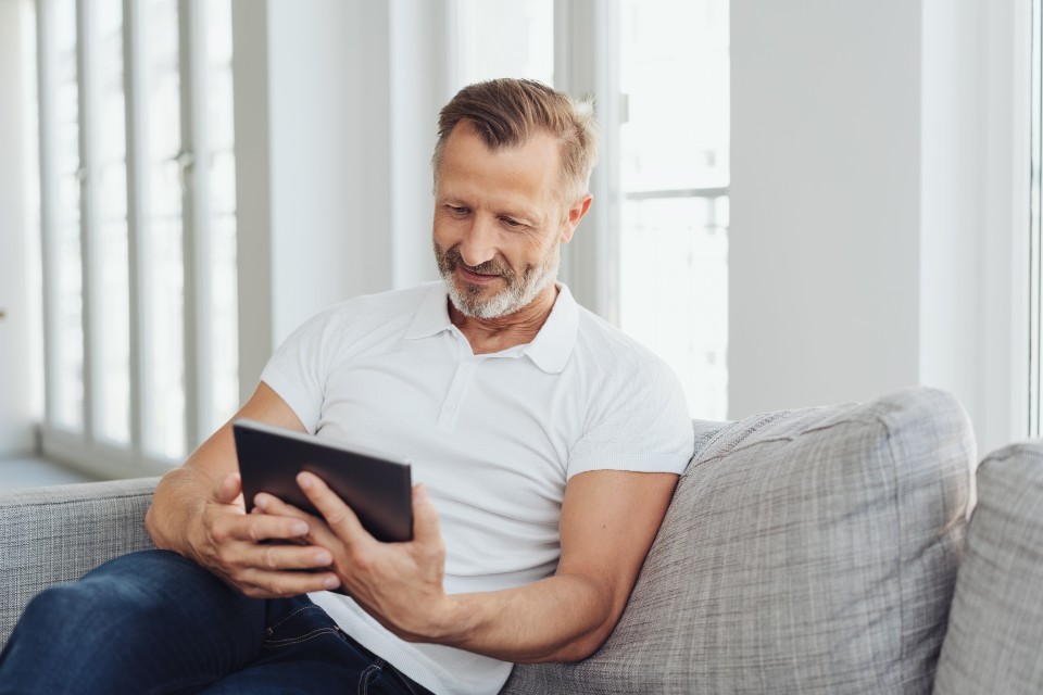 Mature male sitting on sofa holding a tablet