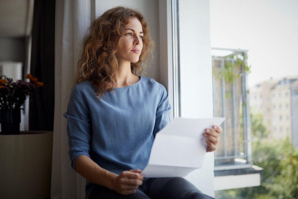 Woman solemnly looking out of window, holding letting in hands 