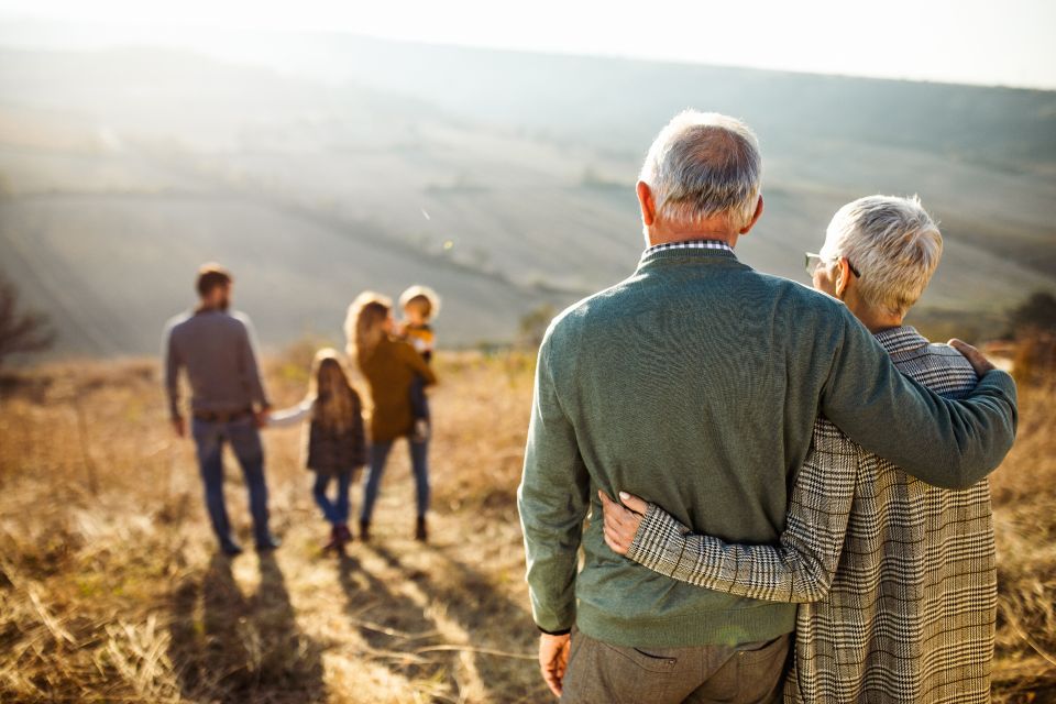 Elderly couple on hill hugging while watching family in distance