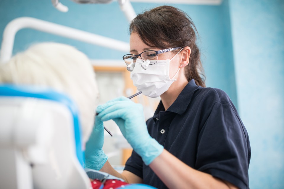 Female dentist wearing glasses and mask treating patient