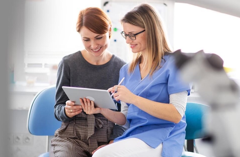 Smiling female dentist sharing the screen of a tablet with a smiling female patient