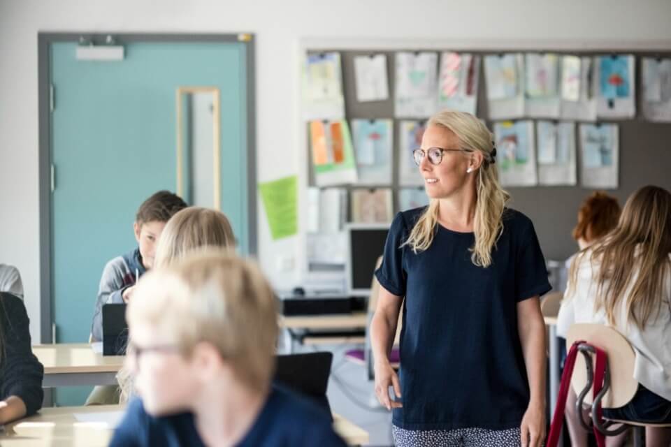 Female teacher walking through classroom filled with students