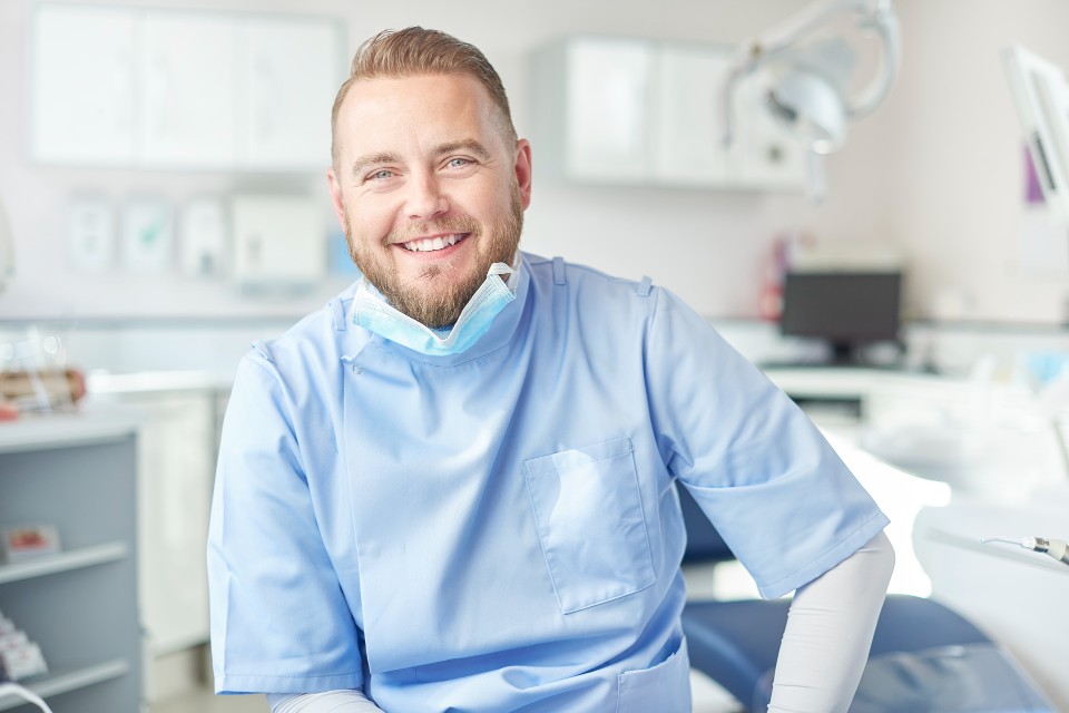 Male dentist wearing scrubs smiling with mask pulled down