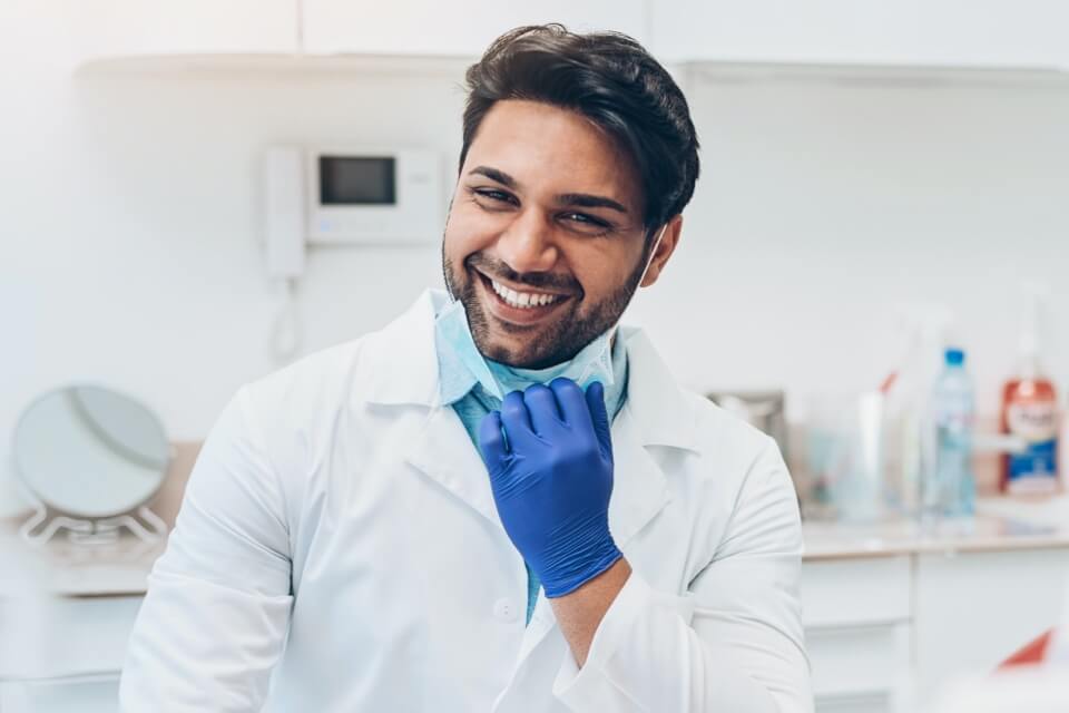Male dentist pulling down mask and smiling