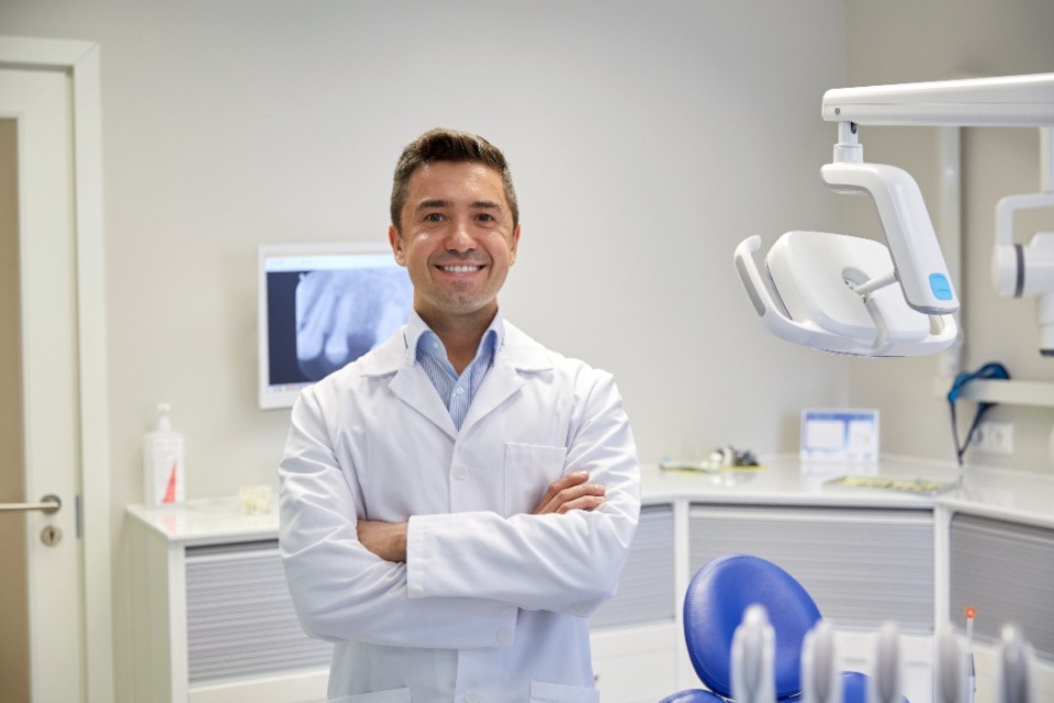 Mature male dentist standing with crossed arms smiling wearing white coat