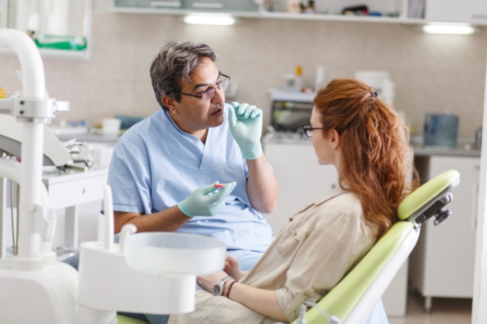 Male dentist in scrubs talking with patient sitting in chair