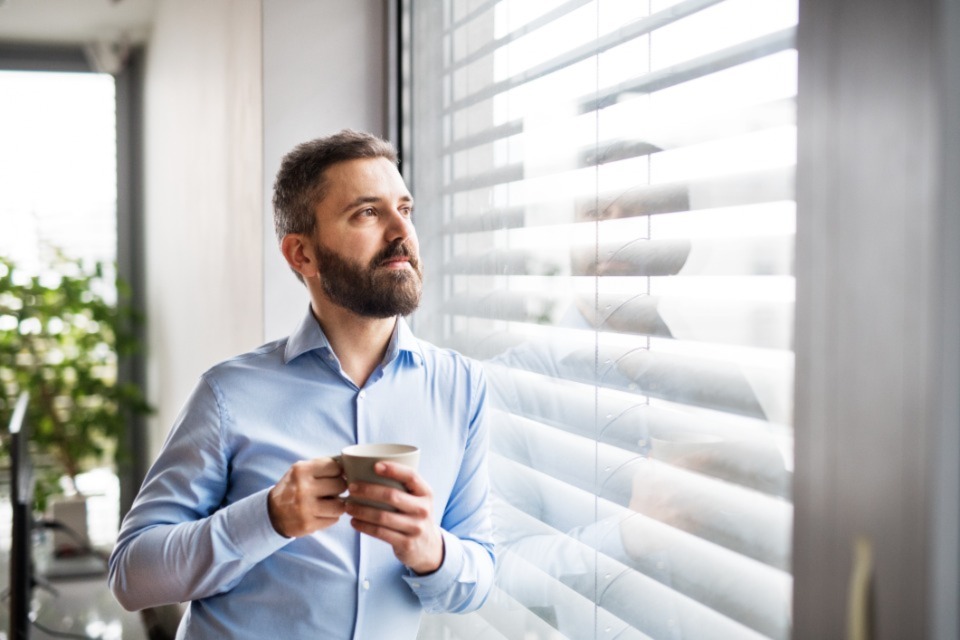 Smartly dressed man looking out of window holding mug