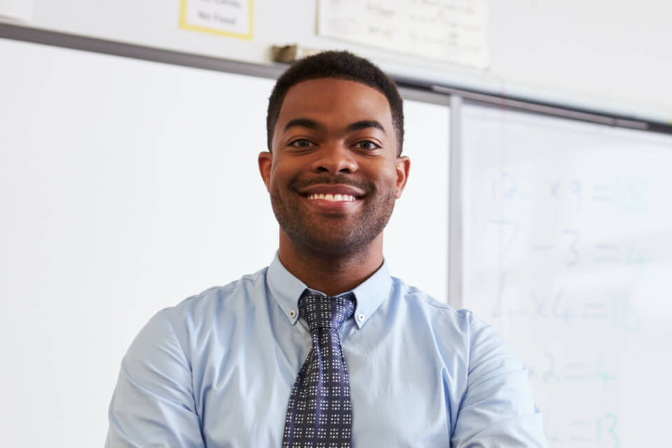 Smiling male teacher standing in front of whiteboard