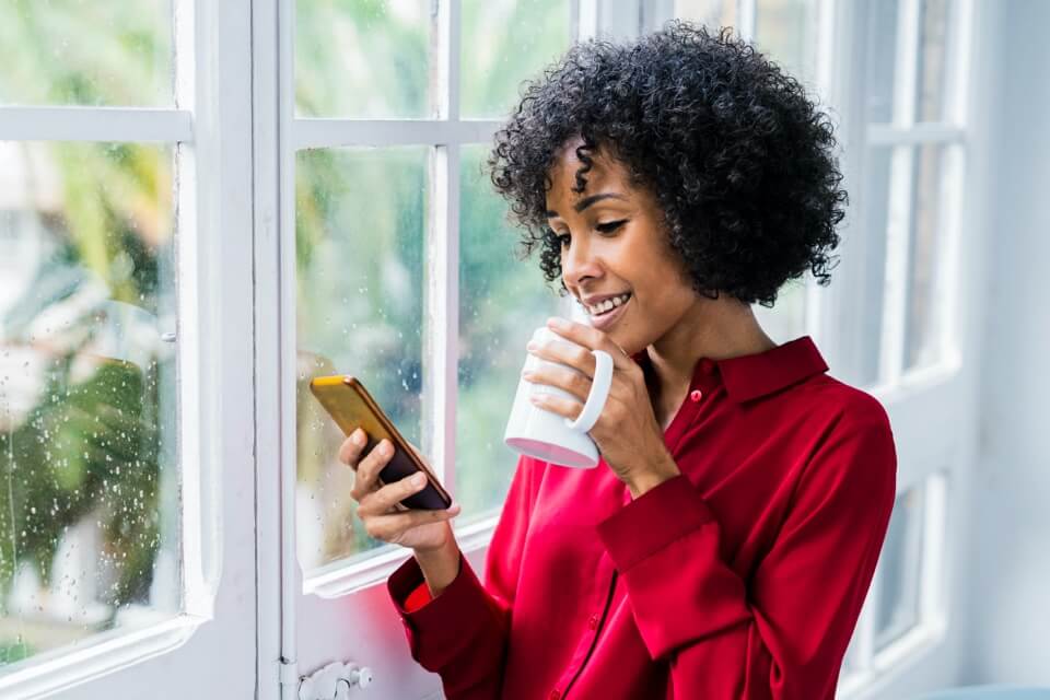 Woman standing in window holding mug and phone