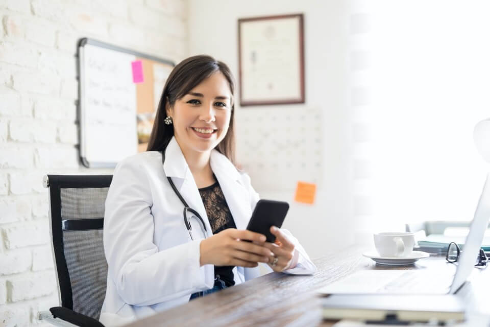 Young female doctor in office holding phone