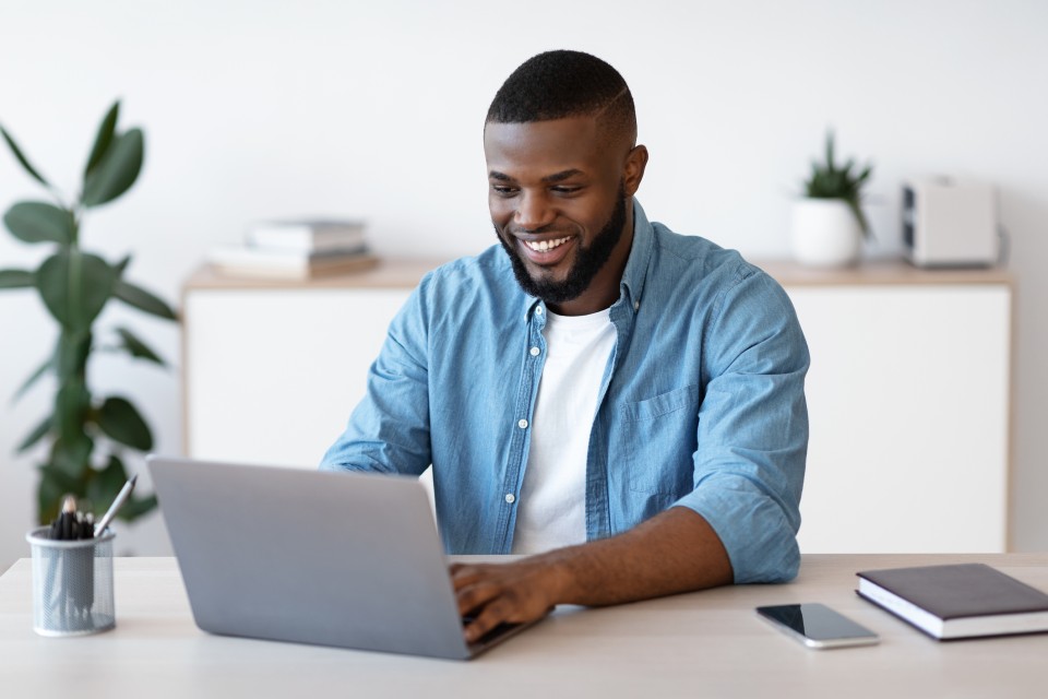 Young male professional sat at desk with laptop smiling