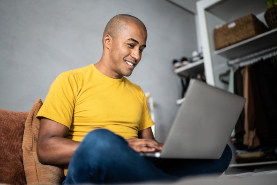 Young male sitting crossed legged in room with laptop smiling