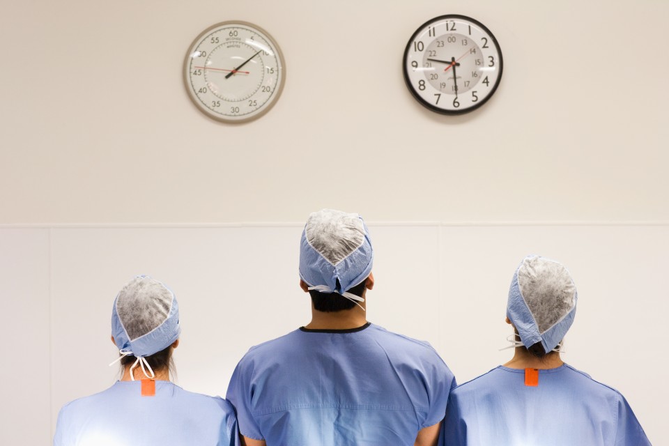 Three medical professionals wearing scrubs standing with backs turned facing wall with two clocks hanging