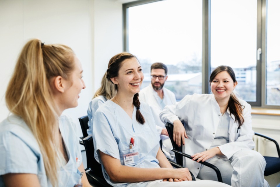 Young female medical professionals wearing scrubs sitting in room together laughing