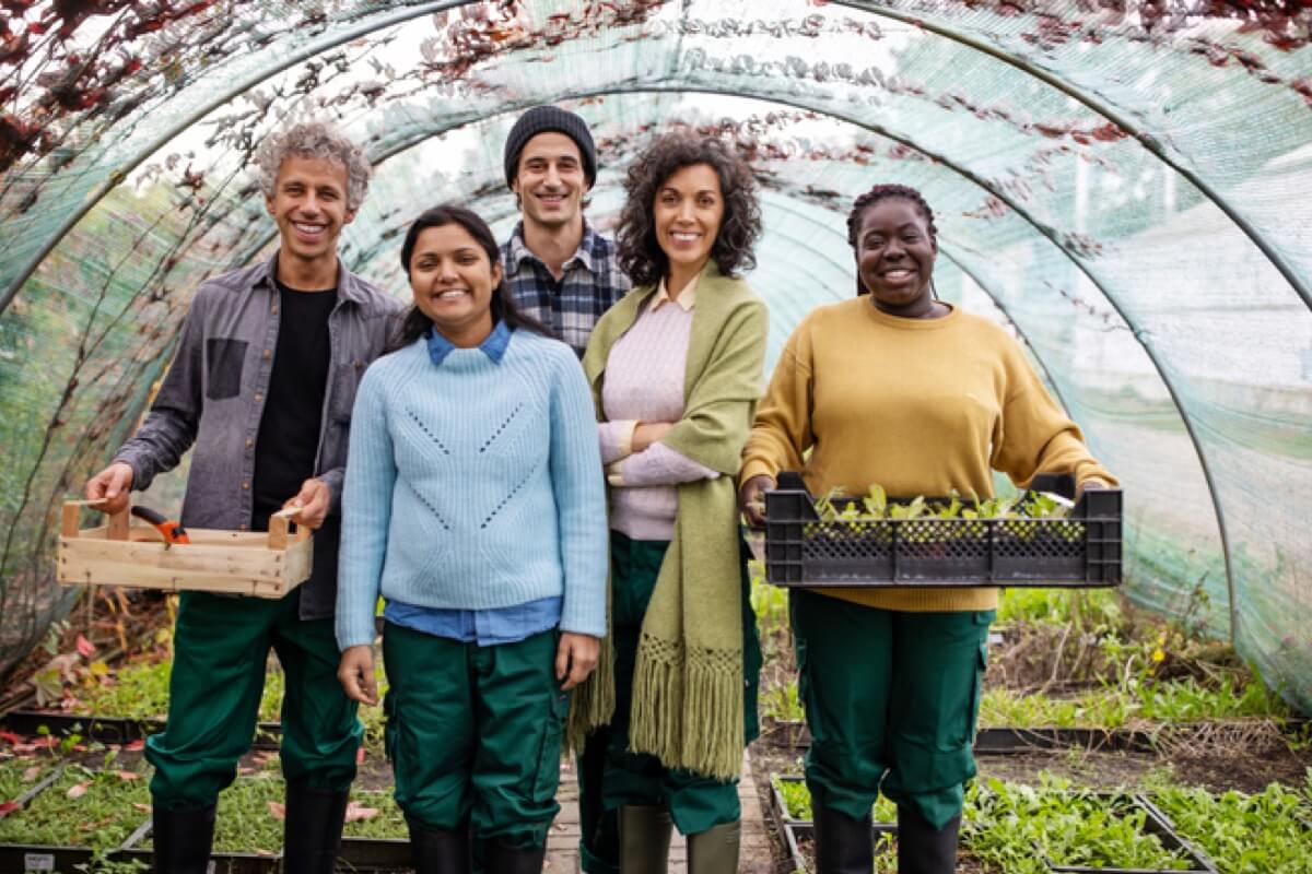 A group of adults stand together in a large greenhouse while smiling A group of adults stand together in a large greenhouse while smiling