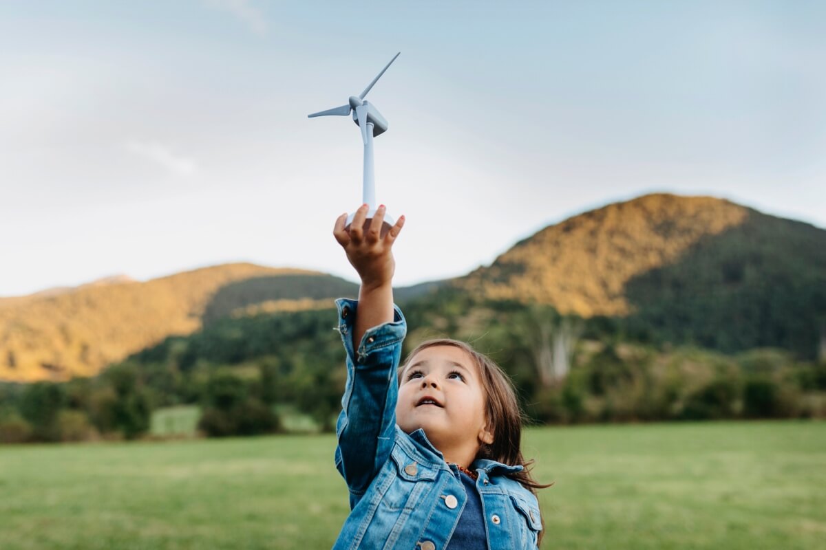 Young child in a field holding up a wind turbine toy