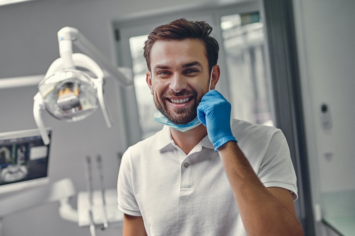 Young male dentist pulling down a mask and smiling in dental room Young male dentist pulling down a mask and smiling in dental room
