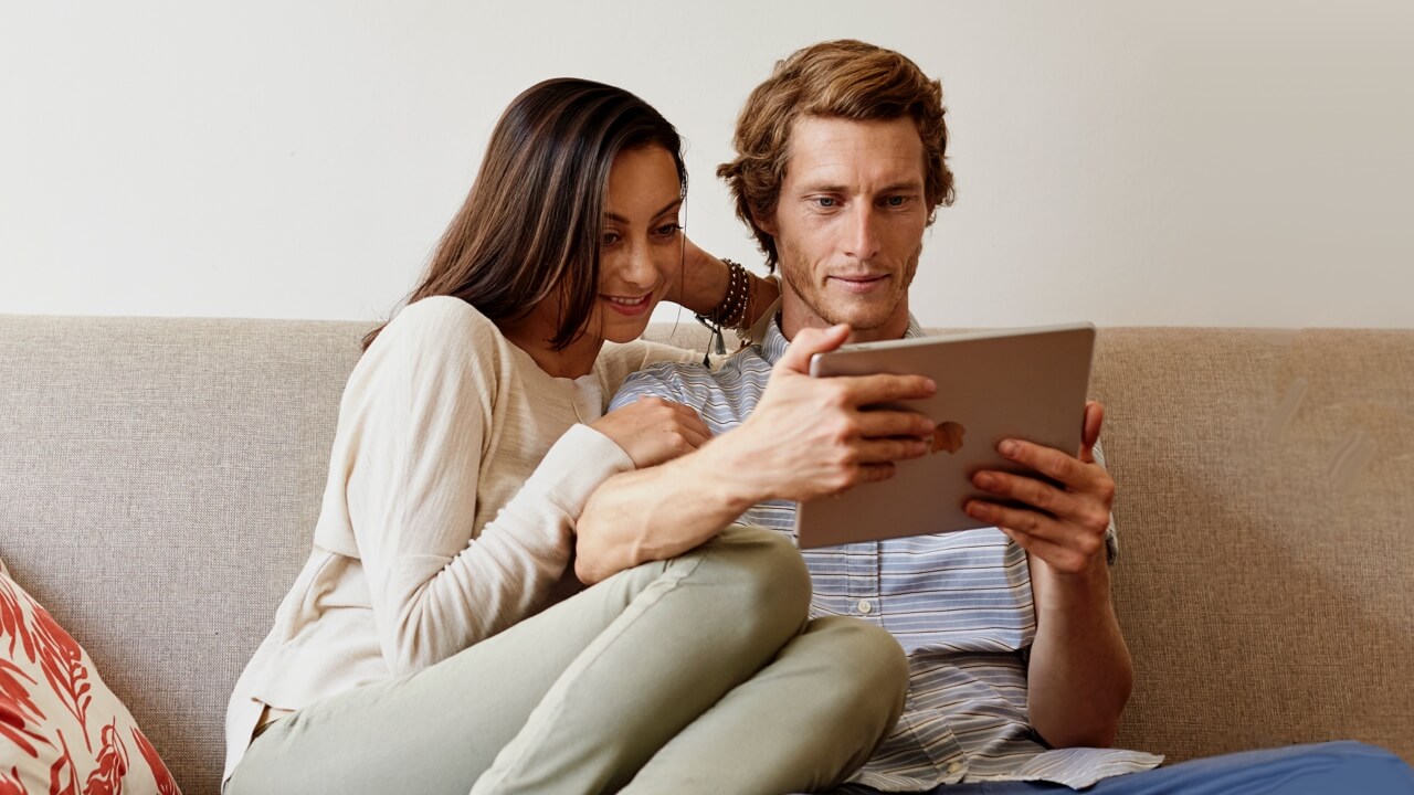 Couple sitting together on sofa looking at ipad Couple sitting together on sofa looking at ipad