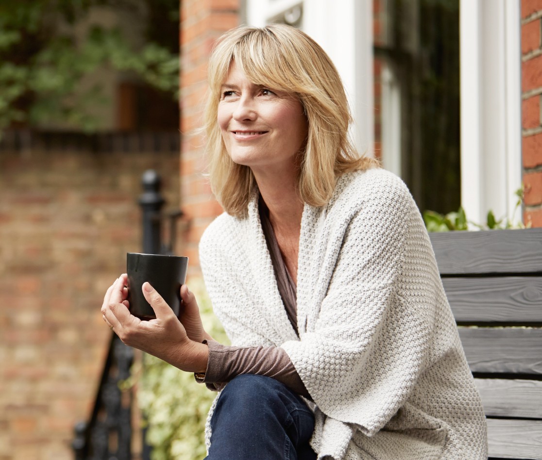 Female sitting outside smiling and holding a mug Female sitting outside smiling and holding a mug