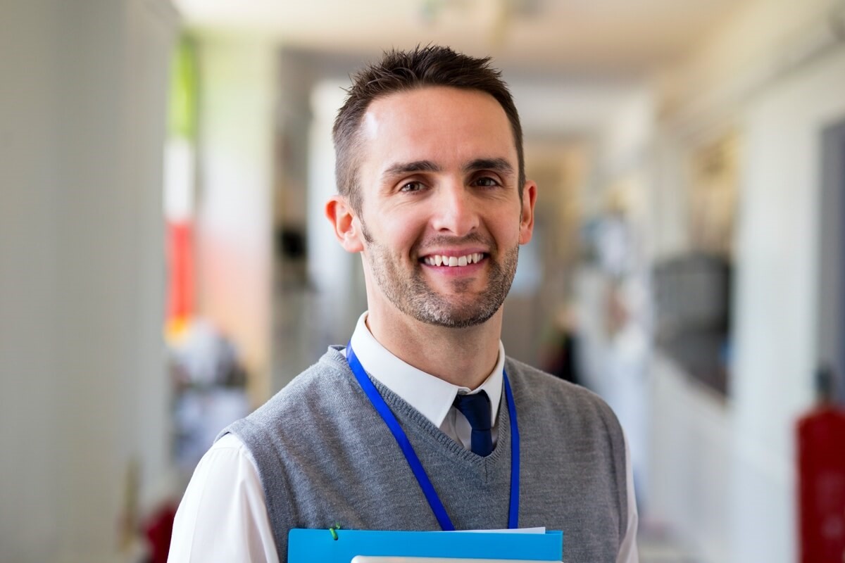 Male teacher smiling holding files Male teacher smiling holding files