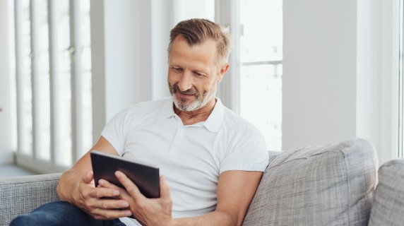 Mature man sitting on sofa holding ipad Mature man sitting on sofa holding ipad