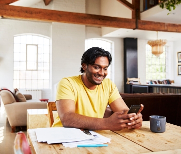 Professional man sitting at desk in home using phone while smiling Professional man sitting at desk in home using phone while smiling