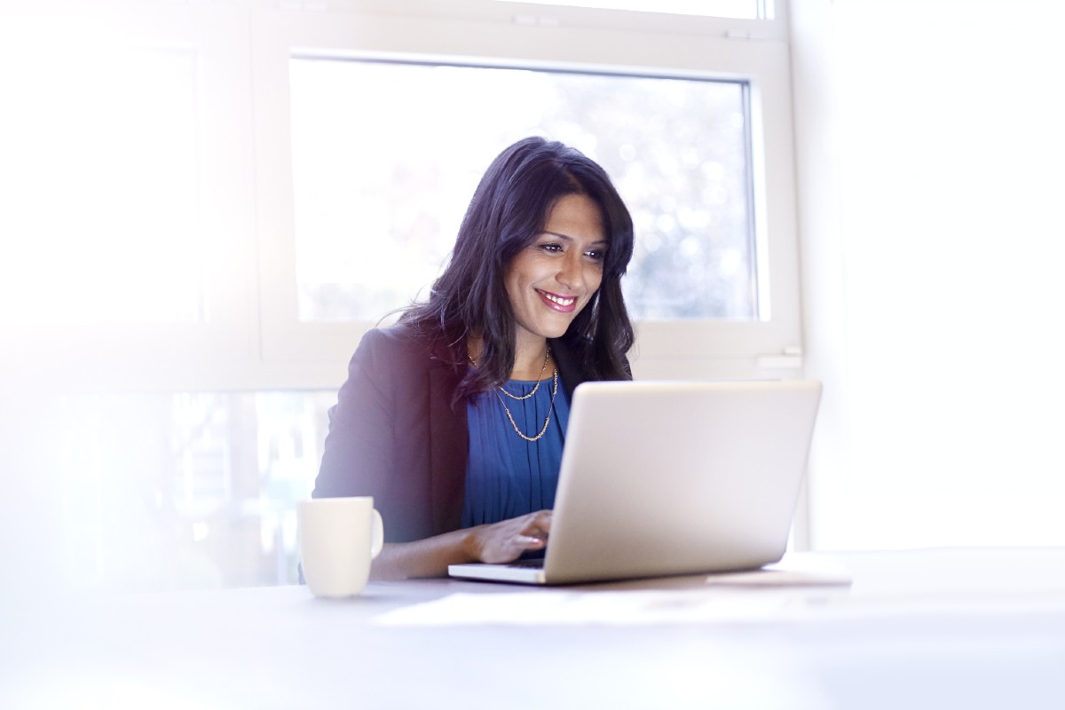 Smartly dressed woman sitting at desk with laptop and mug Smartly dressed woman sitting at desk with laptop and mug