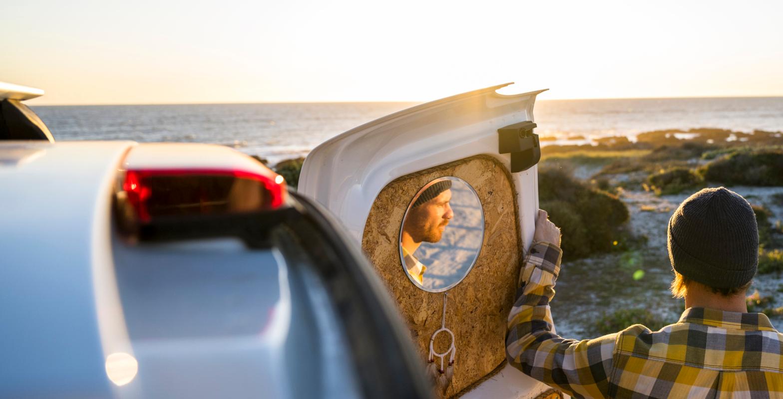 Man standing on a beach leaning on an open van door Man standing on a beach leaning on an open van door watching sunset