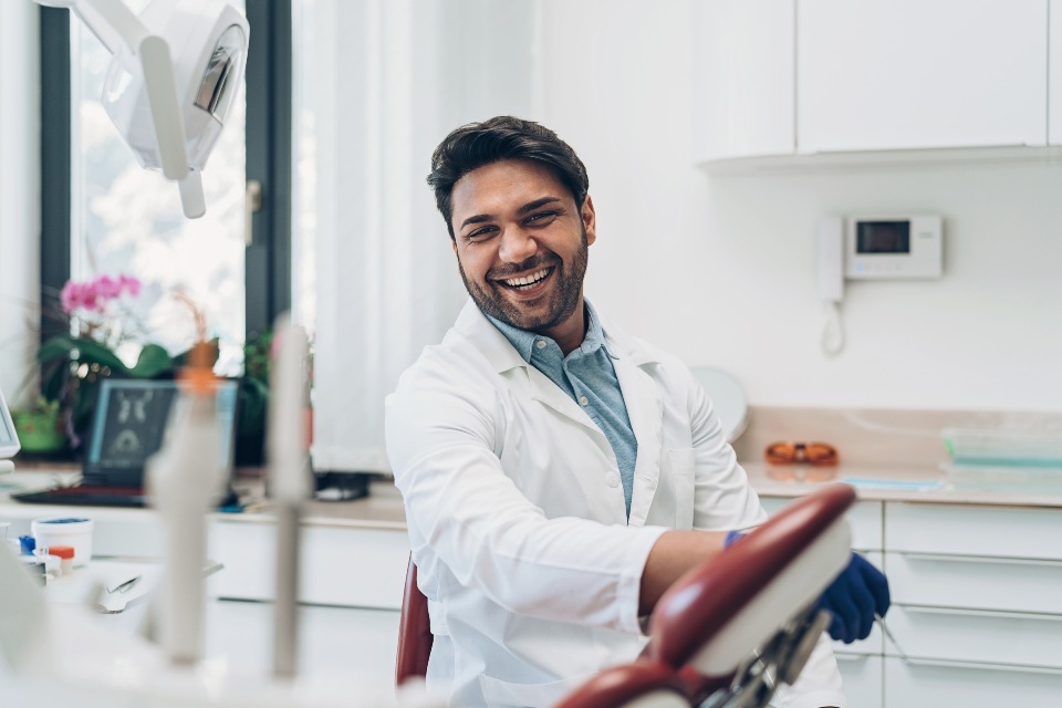 Male dentist wearing white coat in dental room laughing Male dentist wearing white coat in dental room laughing