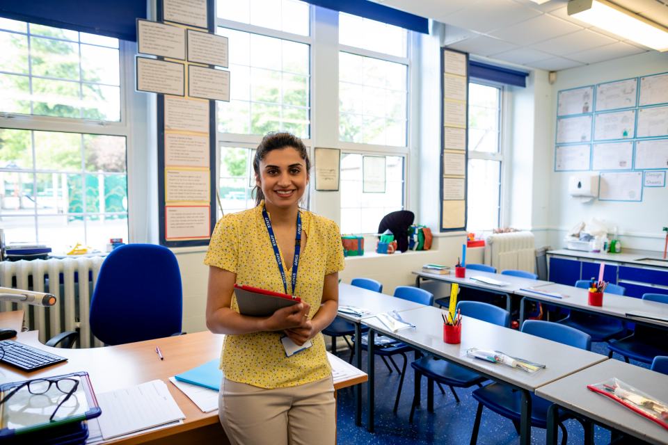 Female teacher leaning on desk in empty classroom