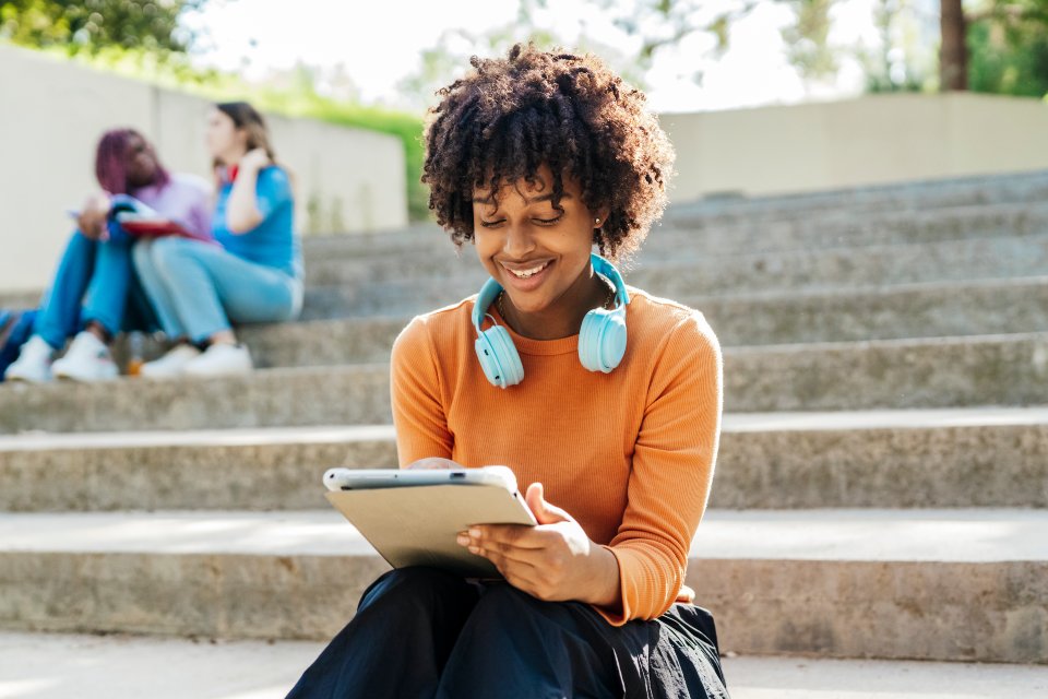 Female student sitting on steps with headphone and tablet