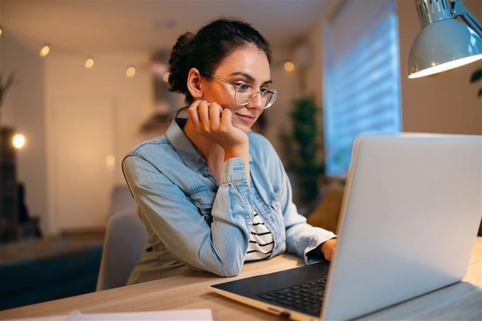 Female student with glasses sitting at desk looking at laptop in home