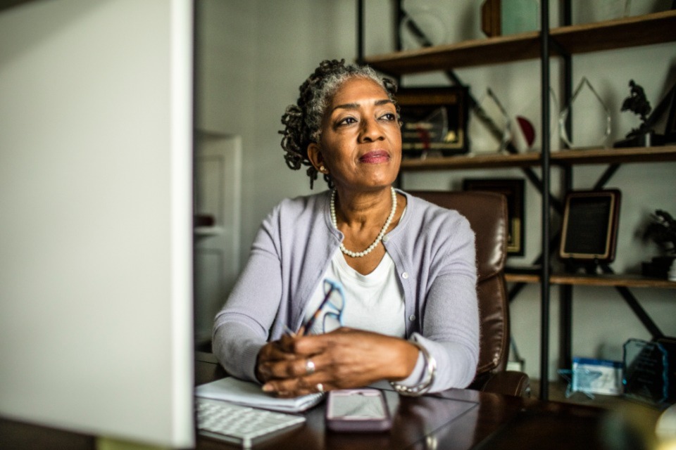 Woman in home office sitting at desk looking out window
