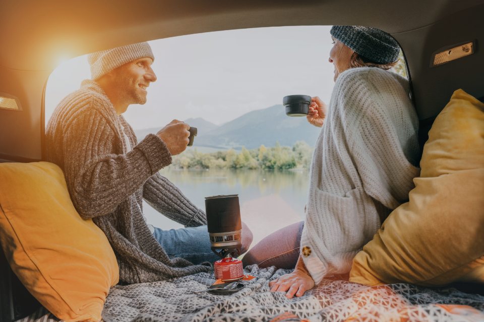 Couple sitting in open camper van drinking from cups