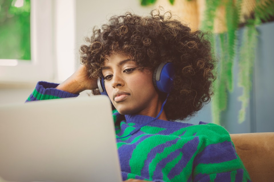 Female student sitting on sofa with laptop wearing headphones