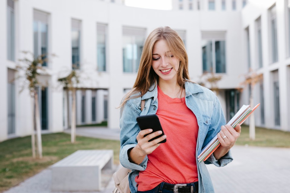 Student walking outside while using phone and smiling