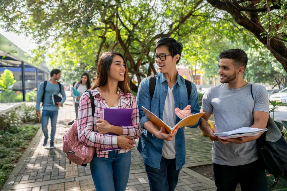 Three students walking outside in conversation while holding paperwork