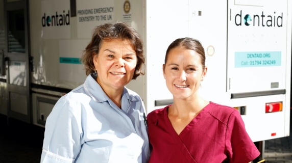 Two nurses in scrubs stand in front of Dentaid van