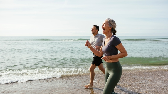 Man and woman happily running on beach in exercise clothes