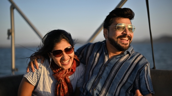 Man and woman sitting on boat wearing sunglasses and laughing