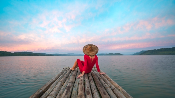Woman sitting on wooden pier wearing a sunhat and looking at sunset