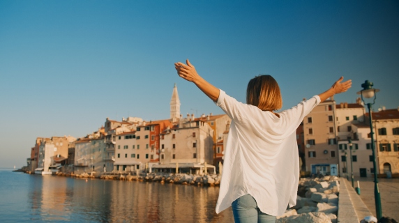 Woman standing on beach front with open arms looking out at sea