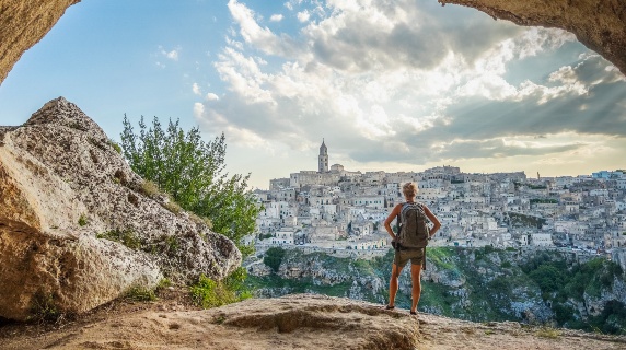 Woman standing on hill with backpack looking at scenic city views