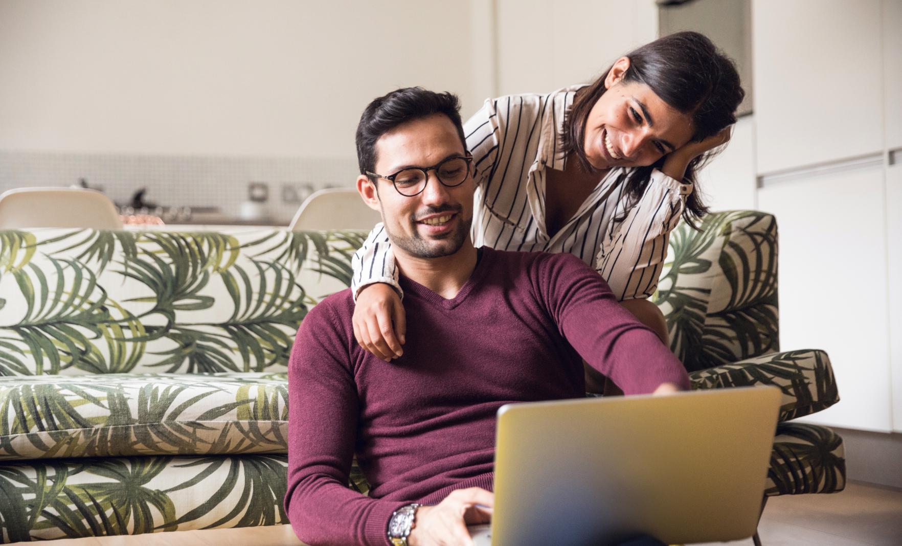 Male sitting on floor and female sitting on sofa looking at laptop