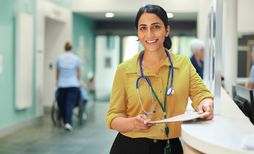Female GP standing in practice leaning on reception desk