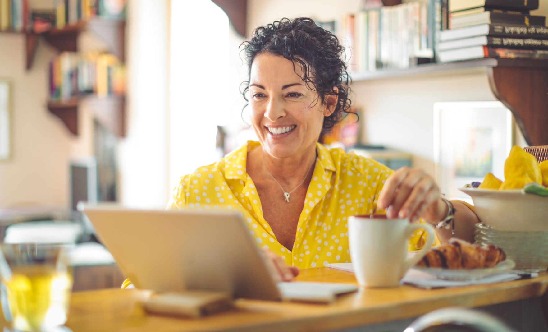Professional female smiling and stirring the mug with a spoon while using tablet