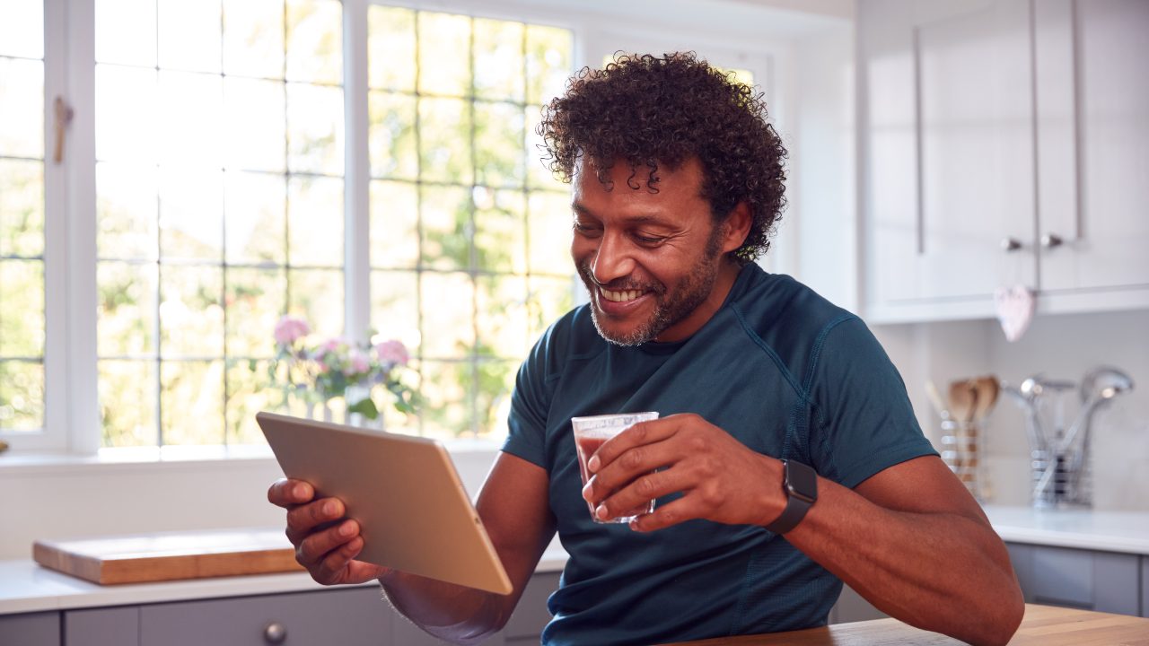 Mature man at kitchen counter with a tablet and coffee