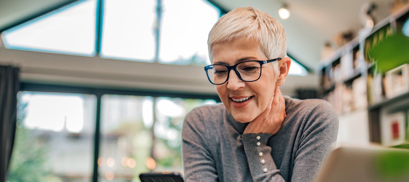 Mature professional woman sitting at desk looking at phone and laptop